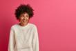 Portrait of dreamy good looking woman with Afro hairstyle, looks away and laughs, discusses funny recent deal at work, has pleasant friendly talk, dressed in casual wear, isolated on pink wall