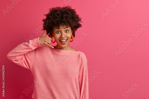 Fotografía Excited female model makes telephone gesture, smiles broadly, dressed in casual