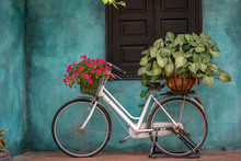 White Vintage Bike With Basket Full Of Flowers Next To An Old Building In Danang, Vietnam