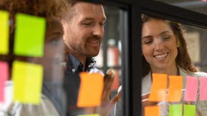 Wall Mural - creative diverse employees team writing ideas on sticky papers on glass wall close up, multiethnic c