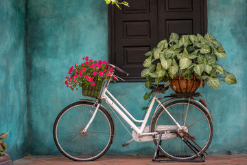 White vintage bike with basket full of flowers next to an old building in Danang, Vietnam