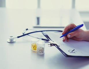 Woman's hands writing on sheet of paper in a clipboard with pen isolated on desk