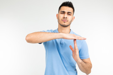 a man in a blue T-shirt shows the letter t with his hands against a studio background