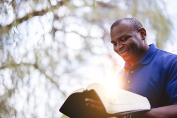 Wall Mural - African-American male reading the Bible and smiling at the park on a sunny day