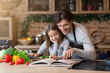 © Prostock-studio - Happy dad and little daughter checking recipe in cookbook together