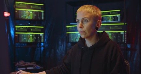 Caucasian woman hacking program via internet while working at night in dark monitoring room. Female anonymous hacker creating computer virus. Cyber crime and safety concept.