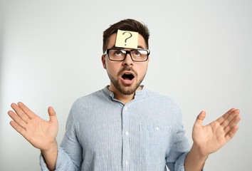 Emotional man with question mark sticker on forehead against light background