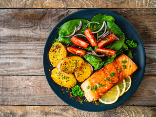 Fried salmon steak with potatoes and vegetables on wooden table