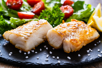 Fish dish - fried cod fillet with vegetables on wooden table