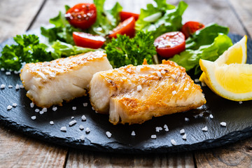 fish dish - fried cod fillet with vegetables on wooden table