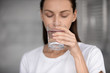 © fizkes - Focus on peaceful young brunette woman drinking glass of fresh aqua, head shot close up. Attractive 30s lady sipping water, enjoying daily healthcare routine, every day healthy habit concept.