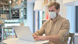 © stockbakers - Young Man with Face Mask using Laptop in Cafe