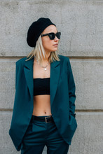 Fashionable Girl In A Turquoise Suit And Black Hat Walks Down The Street. American Girl In A Jacket And Black Cap. Women's Streetwear 