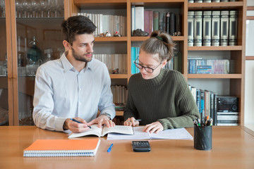 Teacher giving private lessons to a student in a library. Improving through tutoring. 