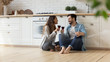 © fizkes - Happy loving couple sitting on warm wooden floor in modern kitchen, drinking red wine, holding glasses, smiling beautiful wife and husband having fun, enjoying romantic date, celebrating event