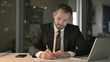 © stockbakers - The Young Businessman Writing document on Office Desk at Night