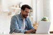 © fizkes - Focused young man wearing glasses using laptop, typing on keyboard, writing email or message, chatting, shopping, successful freelancer working online on computer, sitting in modern kitchen
