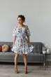 Fashion shot of a young beautiful woman in a short dress posing in the interior. Portrait of a model girl with curly hair and slim body in light spring dress in interior. Spring fashion. Summertime