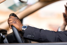 African man in a strict jacket sitting at the wheel of a car, holding the steering wheel close-up