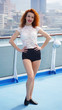 Slim red-haired curly girl posing on the background of the port city and the sea. beautiful green-eyed model smiles at the observation deck. vertical photo, European girl emotions