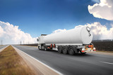 Fototapeta Sport - Big fuel tanker truck shipping fuel on the countryside road in motion against sky