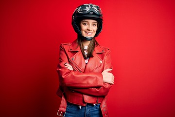 Wall Mural - Young beautiful brunette motocyclist woman wearing motorcycle helmet and red jacket happy face smiling with crossed arms looking at the camera. Positive person.