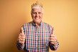 © Krakenimages.com - Senior handsome hoary man wearing golden crown of king over isolated yellow background success sign doing positive gesture with hand, thumbs up smiling and happy. Cheerful expression and winner