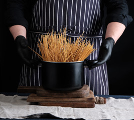 Wall Mural - uncooked yellow long spaghetti in a black metal pan and a chef in a striped apron