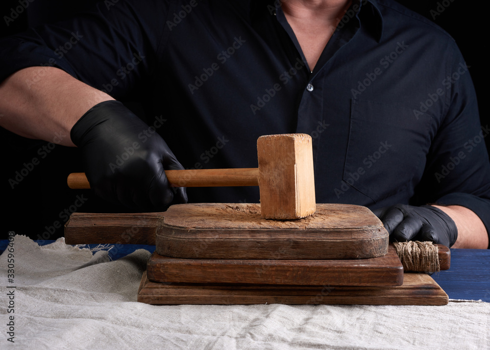 male cook in black uniform holds a wooden hammer for beating meat on a ...