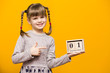 © Svetlana - Close up portrait of first grader girl with funny pigtails smile looking at camera and hold wooden calendar set on 1 september isolated over bright yellow background