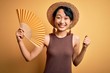 © Krakenimages.com - Young beautiful asian tourist girl on vacation wearing summer hat using hand fan screaming proud and celebrating victory and success very excited, cheering emotion