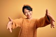 © Krakenimages.com - Young beautiful asian girl wearing casual sweater and diadem standing over yellow background looking at the camera smiling with open arms for hug. Cheerful expression embracing happiness.