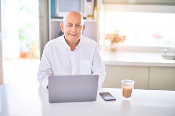 Poster - Senior handsome man smiling happy and confident. Sitting using laptop and drinking cup of coffee at home