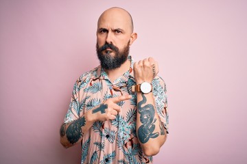 Poster - Handsome bald man with beard and tattoo wearing casual floral shirt over pink background In hurry pointing to watch time, impatience, looking at the camera with relaxed expression