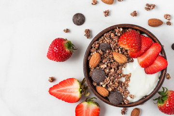 Wall Mural - bowl of oat chocolate granola with yogurt, fresh strawberries and nuts on white marble background for healthy breakfast