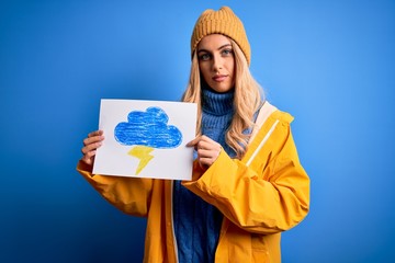 Poster - Young blonde woman wearing raincoat for rainy weather holding paper with clound and thunder with a confident expression on smart face thinking serious