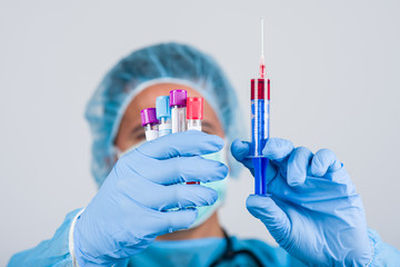 Doctor in medical uniform with a protective face mask and a gloved hand holding syringe and test tube with blood for 2019-nCoV analyzing. Novel Chinese Coronavirus blood test Concept.