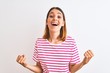 © Krakenimages.com - Beautiful redhead woman wearing casual striped pink t-shirt over isolated background celebrating surprised and amazed for success with arms raised and open eyes. Winner concept.