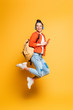 © LIGHTFIELD STUDIOS - excited student in headset and glasses jumping while holding smartphone on yellow background