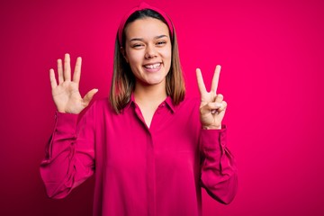 Young beautiful brunette girl wearing casual shirt standing over isolated pink background showing and pointing up with fingers number seven while smiling confident and happy.