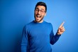 © Krakenimages.com - Young handsome man with beard wearing casual sweater and glasses over blue background with a big smile on face, pointing with hand finger to the side looking at the camera.