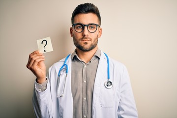 Wall Mural - Young doctor man wearing stethoscope holding question mark reminder over isolated background with a confident expression on smart face thinking serious