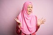 © Krakenimages.com - Young beautiful girl wearing muslim hijab standing over isolated pink background celebrating mad and crazy for success with arms raised and closed eyes screaming excited. Winner concept