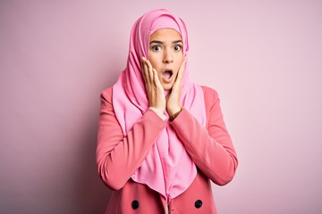 Poster - Young beautiful girl wearing muslim hijab standing over isolated pink background afraid and shocked, surprise and amazed expression with hands on face