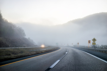 Foggy mist road highway driving with headlights in rural countryside in West Virginia with cars and entrance to clouds