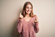 © Krakenimages.com - Young beautiful redhead woman wearing pink casual sweater over isolated white background doing money gesture with hands, asking for salary payment, millionaire business