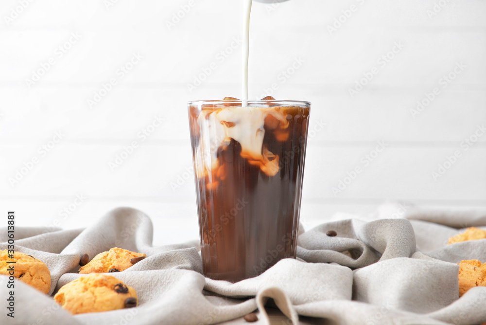 Pouring of milk into cold coffee in glass on table