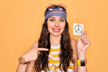 Wall Mural - Beautiful hippie woman with blue eyes wearing sunnglasses holding peace symbol reminder with surprise face pointing finger to himself