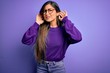 © Krakenimages.com - Young beautiful smart woman wearing glasses over purple isolated background Trying to hear both hands on ear gesture, curious for gossip. Hearing problem, deaf