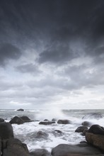Vertical Shot Of A Sea With Waves Hitting The Rocks Under A Cloudy Sky - Great For A Background